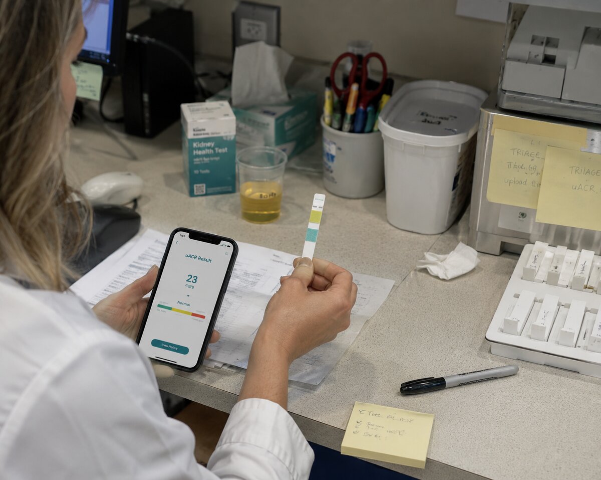 A clinician reading an at-home uACR result on a phone beside a Siemens test strip.